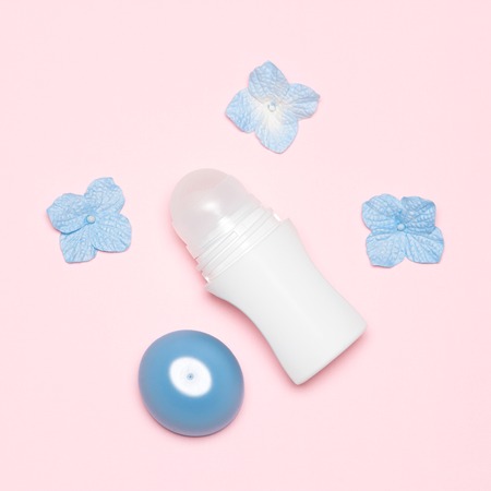 Open bottle of body antiperspirant deodorant roll-on with flowers, top view