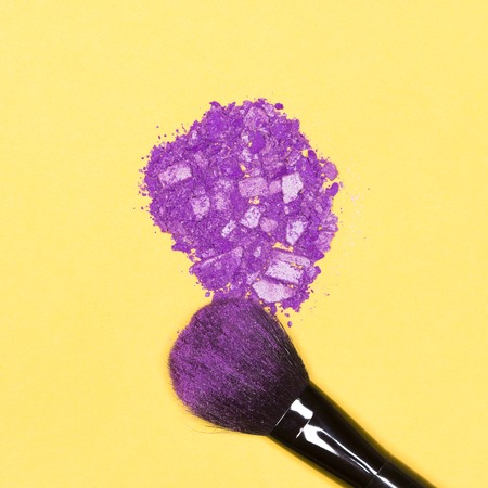 Close-up of makeup brush with crumbled violet eye shadow on bright yellow backgroundの写真素材