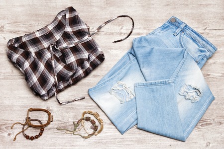 Hippie fashion style women outfit. Cotton check shirt, ripped jeans, rope wood bead bracelets on shabby wooden backgroundの写真素材