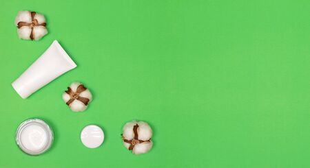 Beauty cosmetic products with cotton flowers on green background. Top view, flat lay. Copy space. Natural cosmetics with cotton extract conceptの写真素材