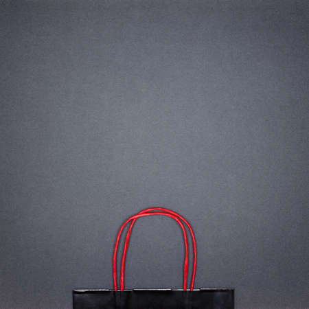 Black paper shopping bag on dark gray background. Copy space. Black Friday sale minimal concept