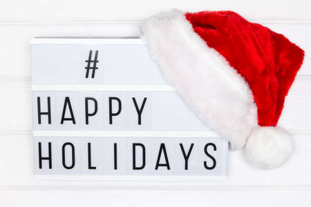 Happy holidays hashtag on white lightbox with red Santa hatの写真素材