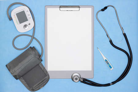 Blank patient medical history, blood pressure monitor, stethoscope, thermometer on blue desk....