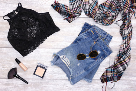 Blue ripped denim shorts, black lace bra, scarf, sunglasses with foundation fluid and face powder. Fashion women clothes and make-up products. Summer essentialsの写真素材