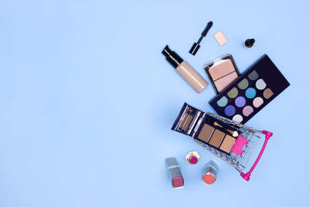 Make-up products with shopping cart on blue background. Makeup cosmetics sale concept. Copy spaceの写真素材