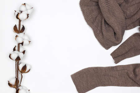 Warm brown wool sweater with white cotton flower sprig on white background top view. Cozy winter wear. copy spaceの写真素材