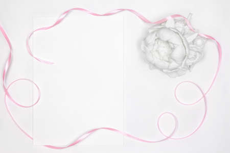 White rose decor and blank white paper card with pink satin ribbon on white background. copyspace. wedding mock-upの写真素材