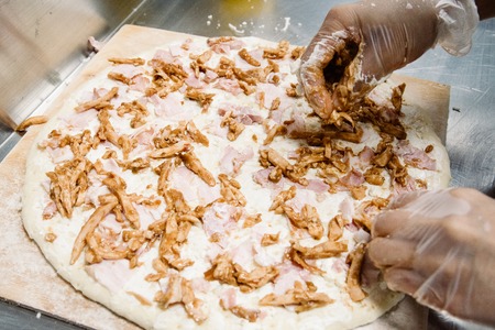 Female hands in latex gloves making, decorating pizza.