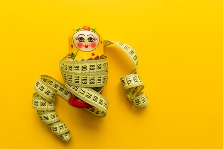 nesting doll matrioshka with tailor's meter on orange background. minimal concept. top view.の写真素材