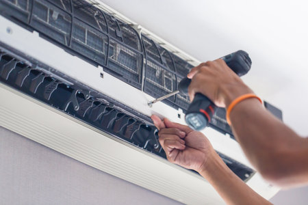 Repairman using a screwdriver fixing modern air conditioner, Male technician cleaning air conditioner indoors, Maintenance and repairing conceptsの写真素材