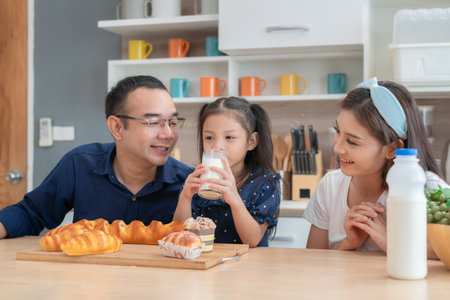 Asian family of father, mother and daughter enjoying breakfast together in kitchen, Kid girl drinking milkの写真素材