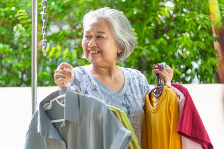 Smiling senior woman holding drying clothes from washing line in backyardの写真素材