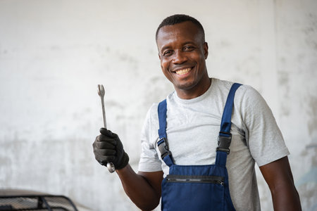 Happy Mechanic with Wrench in Workshop, Smiling African American Tradesman Ready to Work, Professional Repairman Holding Tool Looking at Cameraの写真素材