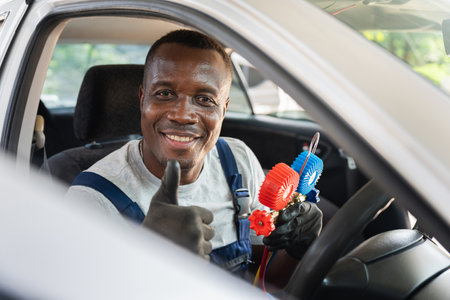 Smiling Mechanic in Car Holding AC Gauges, Happy Auto Technician Giving Thumbs Up, Professional Car...