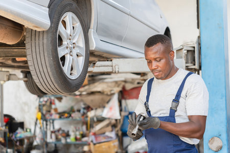 Automotive Technician Examining Car Parts in Garage, Mechanic Working on Vehicle Lift, Focused Repairman During Car Inspectionの写真素材