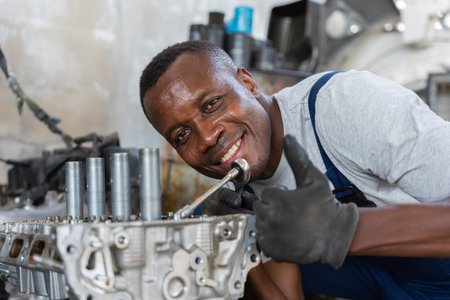 Smiling African American Mechanic Working on an Engine, Auto Repair Technician Giving Thumbs Up in Garage, Happy Engineer Assembling Car Parts with Toolsの写真素材