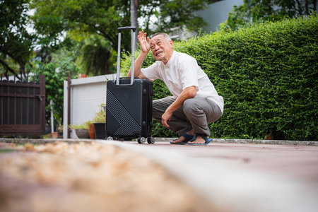 Senior Man Sweating with Luggage Outdoors, Exhausted Senior Man Wiping Sweat Next to Luggage Outdoors, Tired Elderly Traveler, Mature Man Feeling Overwhelmed While Moving Suitcaseの写真素材