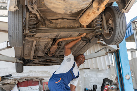 Auto Mechanic Inspecting Undercarriage of Car on Lift, Technician Working Underneath a Vehicle in a Garage, Car Repairman Checking Suspension and Exhaust Systemの写真素材