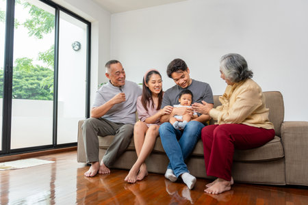 Happy Multi-Generational Family with Baby Smiling on Sofa, Joyful Grandparents, Parents, and Infant Bonding at Home, Asian Family Gathering Three Generations Sharing Laughterの写真素材
