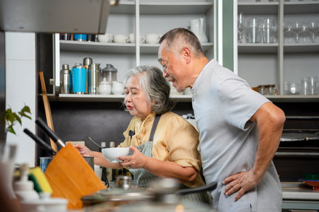Senior Asian Couple Cooking and Tasting Food in Kitchen, Elderly Man and Woman Collaborating on a Meal at Home, Happy Grandparents Enjoying Culinary Activity Togetherの写真素材