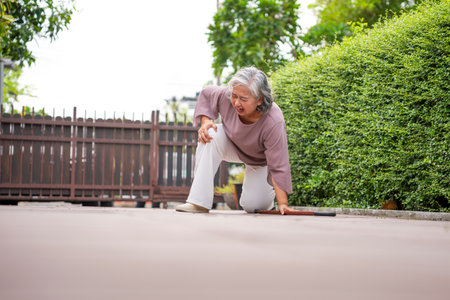 Accidental Fall of a Mature Woman on a Paved Path, Senior Asian Woman Falling Down Outdoors Due to Accident or Weakness, Elderly Woman Collapses While Walking, Needing Assistanceの写真素材