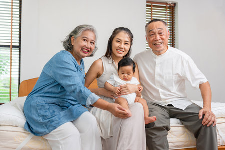 Joyful Asian Family Bonding on Bed, Grandparents, Mother, and Baby Smiling Together, Happy Three Generations Family Portrait at Homeの写真素材