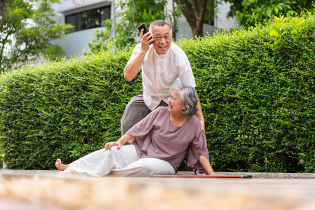Senior Man Helping Fallen Woman Outdoors, Concerned Husband Assistant Wife Who Has Fallen on Pavement, Elderly Asian Couple Facing a Medical Emergency Outside Their Homeの写真素材
