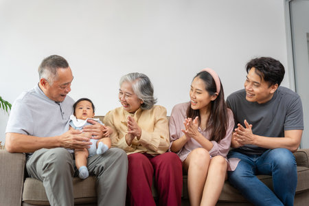 Happy Multi-Generational Asian Family on Sofa at Home, Joyful Grandparents, Parents, and Baby Bonding Together, Three Generations of Asian Family Relaxing and Smilingの写真素材