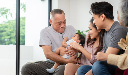 Portrait of Happy Asian Family at Home, Cheerful Grandparents, Parents, and Baby Bonding on Sofa, Multi-Generational Asian Family Smiling Together at Homeの写真素材