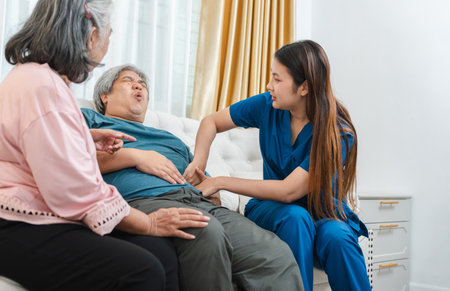Home Care Nurse Examining Senior Male Patient's Abdomen with Concerned Wife, Healthcare Professional...