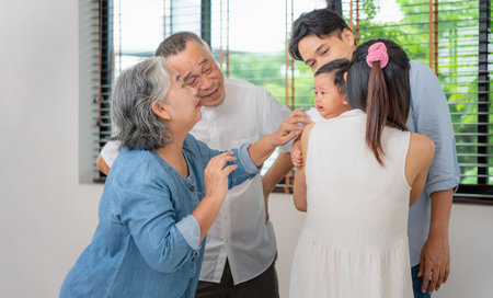 Asian multigenerational family comforting crying baby at home, Grandparents supporting young parents with newborn care, Family bonding moment with grandparents helping soothe babyの写真素材