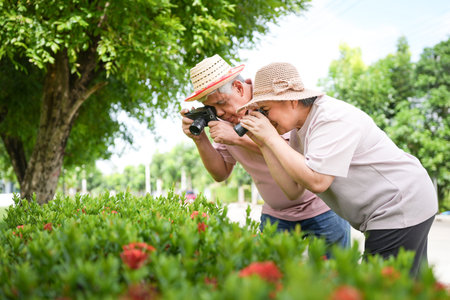 Happy senior couple taking photos of flowers in green garden, Elderly asian couple enjoying...