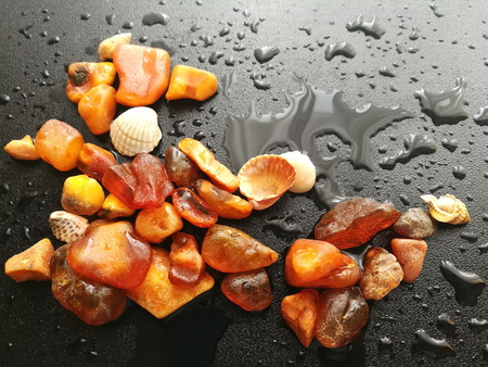 A piece of natural amber of different fractions on a dark background with raindrops.の写真素材