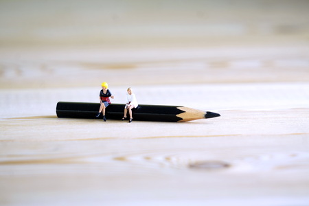 Miniature figures of two women sitting on a pencil. The concept of discussing the problem at lunch.の写真素材