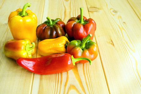 Red, yellow, green bell pepper on light wooden background.