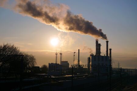 Morning dawn in a factory with industrial pipes and smoke. Pollution of the urban atmosphere....