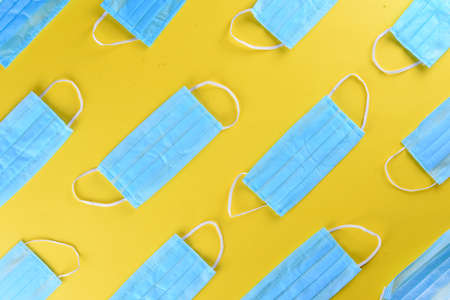 A flat lay photo of blue surgical mask in yellow backdropの写真素材