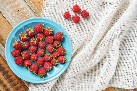 Red raspberry in blue dish and in front of white fabric on old vintage wooden table.の写真素材