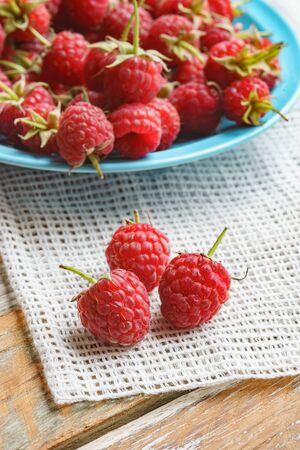 Red raspberry in blue dish and in front of white fabric on old vintage wooden table.の写真素材
