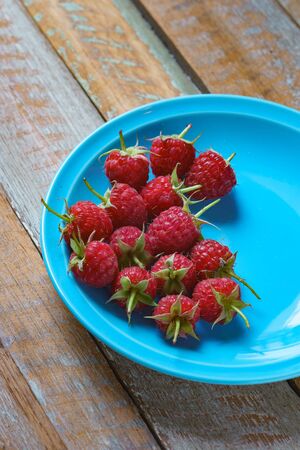 Red raspberry in blue green dish on old vintage wooden table.の写真素材