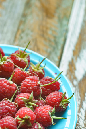 Red raspberry in blue dish on old vintage wooden table.の写真素材