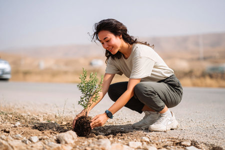 young woman planting a tree in a barren area, symbol of renewal and sustainable aidの素材