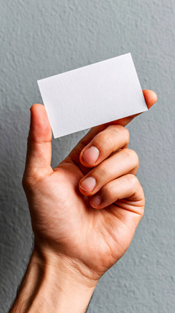 Hand holding blank white card shown close-up on a gray backdropの素材