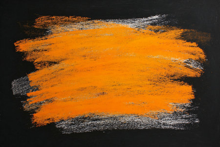 Blackboard marked with orange and white chalk smudges on dark backgroundの素材