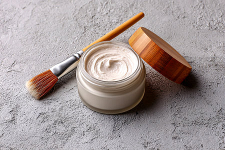 Beige and white cosmetic cream with brush placed on textured surfaceの素材