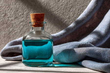 Teal glass bottle with cork resting on textured fabric under soft natural lightの素材