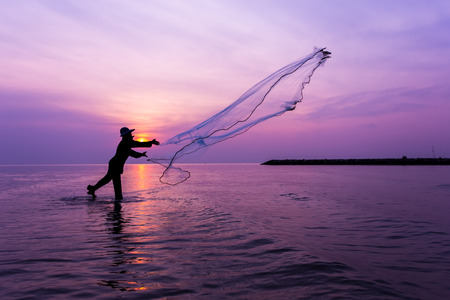 Silhouette of fisherman throwing net at sunset.の写真素材