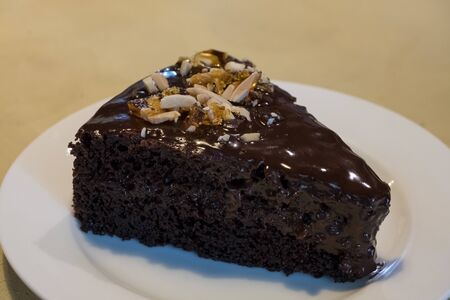 A piece of dark chocolate cake on a plate on a table close-up.