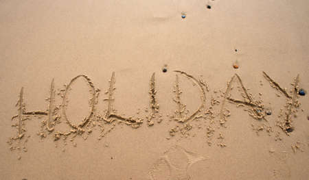 The word Holiday written in sand next to the shoreの写真素材