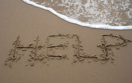 The word Help written in sand next to the shore with a wave washing overの写真素材